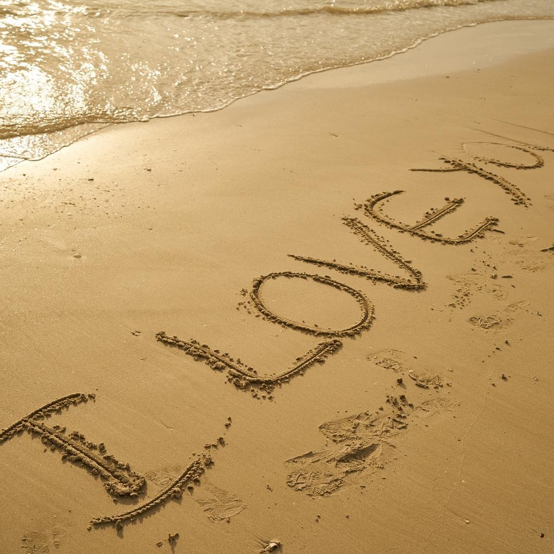 Imagem de uma frase escrita na areia da praia se referindo a Playlist Amor I love you